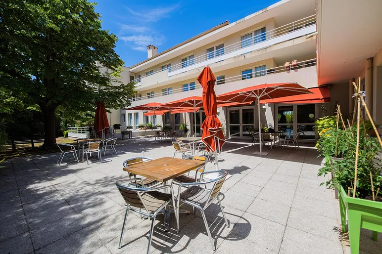 Terrasse avec tables et chaises en bois pour jardin, avec parasols rouges en ehpad à Marseille, Résidence Mazargues