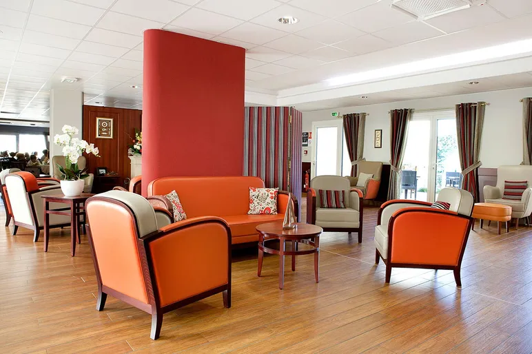 Salle commune détente sofa orange et boisé lumineux en maison de retraite à Le Rove, La Carrairade
