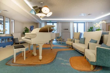 salle de détente cocooning avec grand piano blanc à queue fauteils blanc crème et turquoise lumineuse décorées