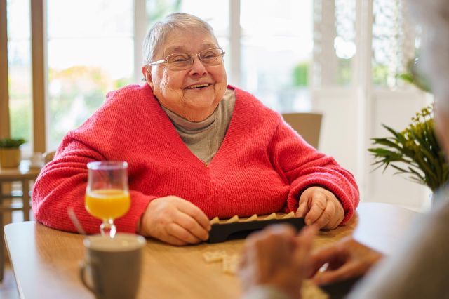 Personne agée avec pull rouge sourire jouant domino jus d'orange Les Jardins d'Epinay