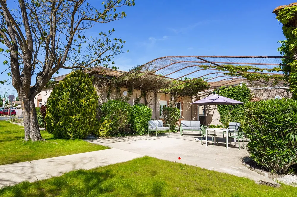 plan cour intérieur jardin avec parasol et chaises et tables, canapé jardin, verdure Les Sereins à Cheval-Blanc