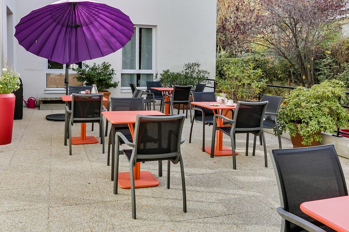 Terrasse extérieur avec tables oranges, chaises noires, EHPAD le Cap
