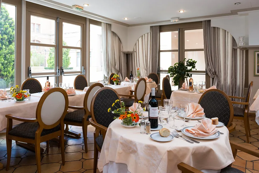 salle de restaurant lumineuse chic et sobre avec tables dressées et decorées, grande fenetre et rideaux marron