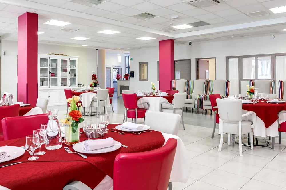 Grande salle avec tables rondes dressés avec fleurs et décorations rouges et blanc, fauteuil rouge grenade