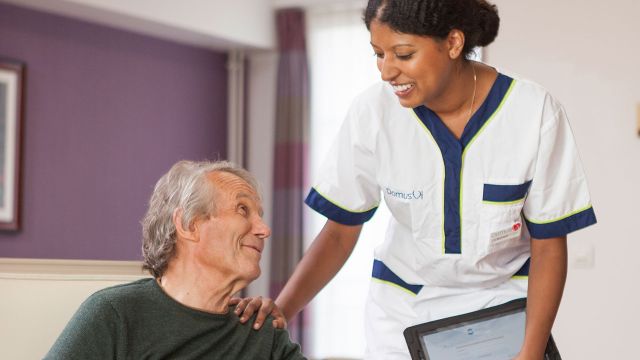 une ergothérapeute pose la main sur l'épaule d'un résident en maison de retraite