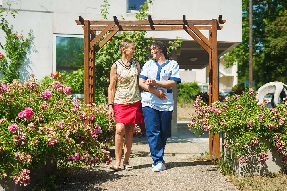 aide soignate avec résident promenande dans le jardin floral soleil et beau temps maison retraite Résidence du Parc à Maisons-Laffitte
