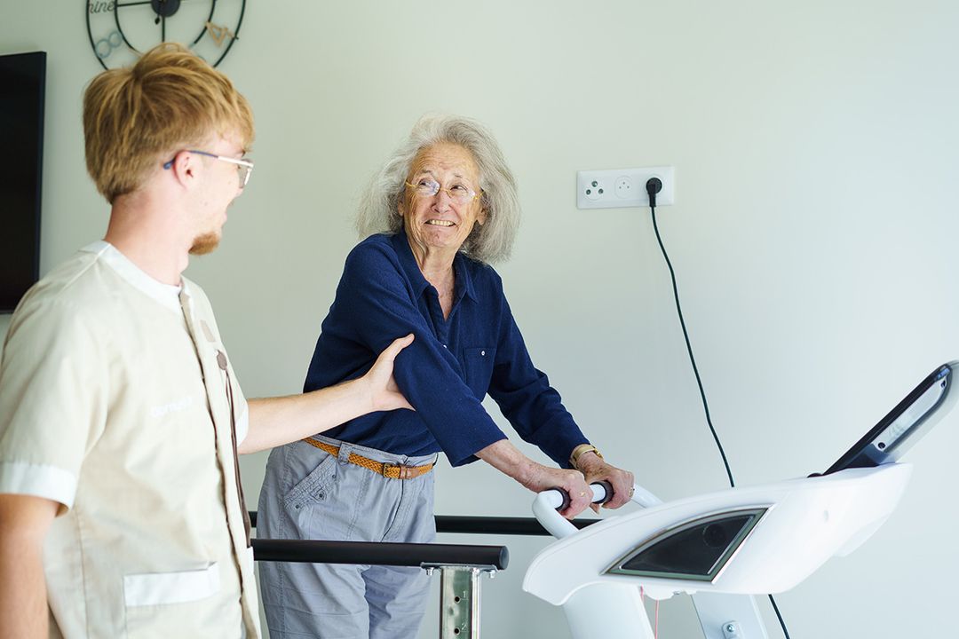 Aide soignant qui assiste une femme âgé sur un tapis de marche résidence seniors à meschers