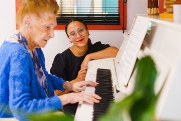 Piano blanc La Fontaine Médicis à Gouvieux avec professeur de piano et résidente agée pull bleu