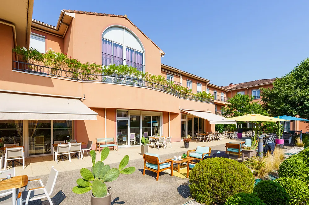 Terrasse extérieure avec tables, chaises, verdure et parasols residence villa des saules
