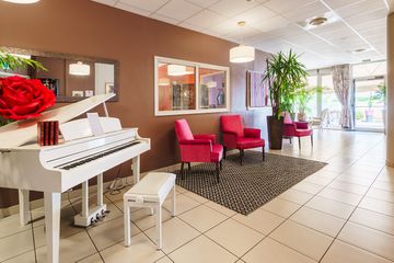 hall lumineux avec un piano blanc, chaises rouges et tapis residence le cannet