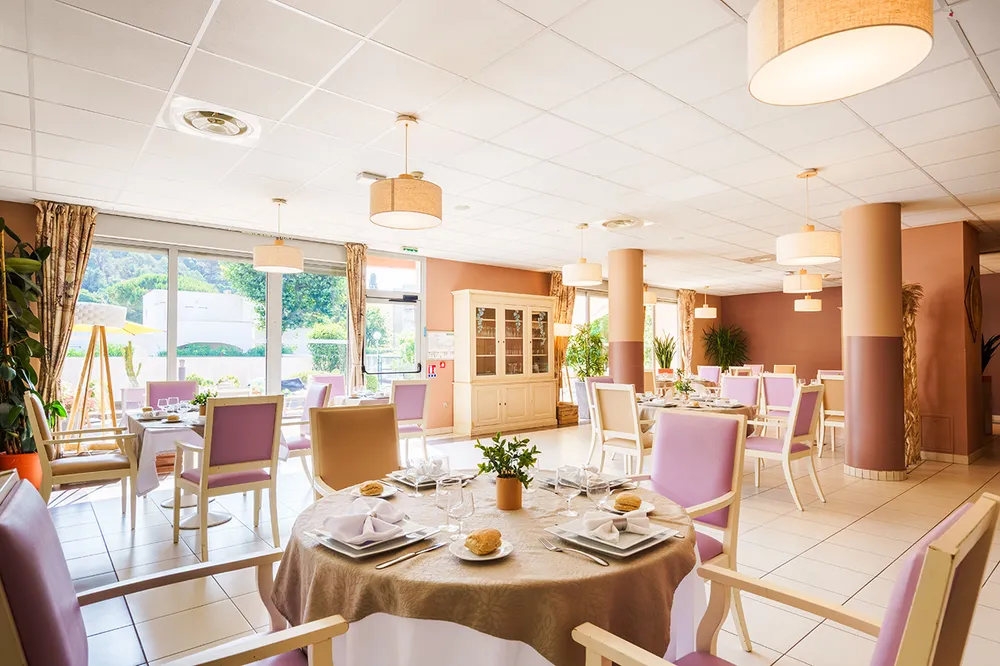 Salle à manger lumineuse avec tables rondes dressées, vaisselles blanches ehpad villa saules