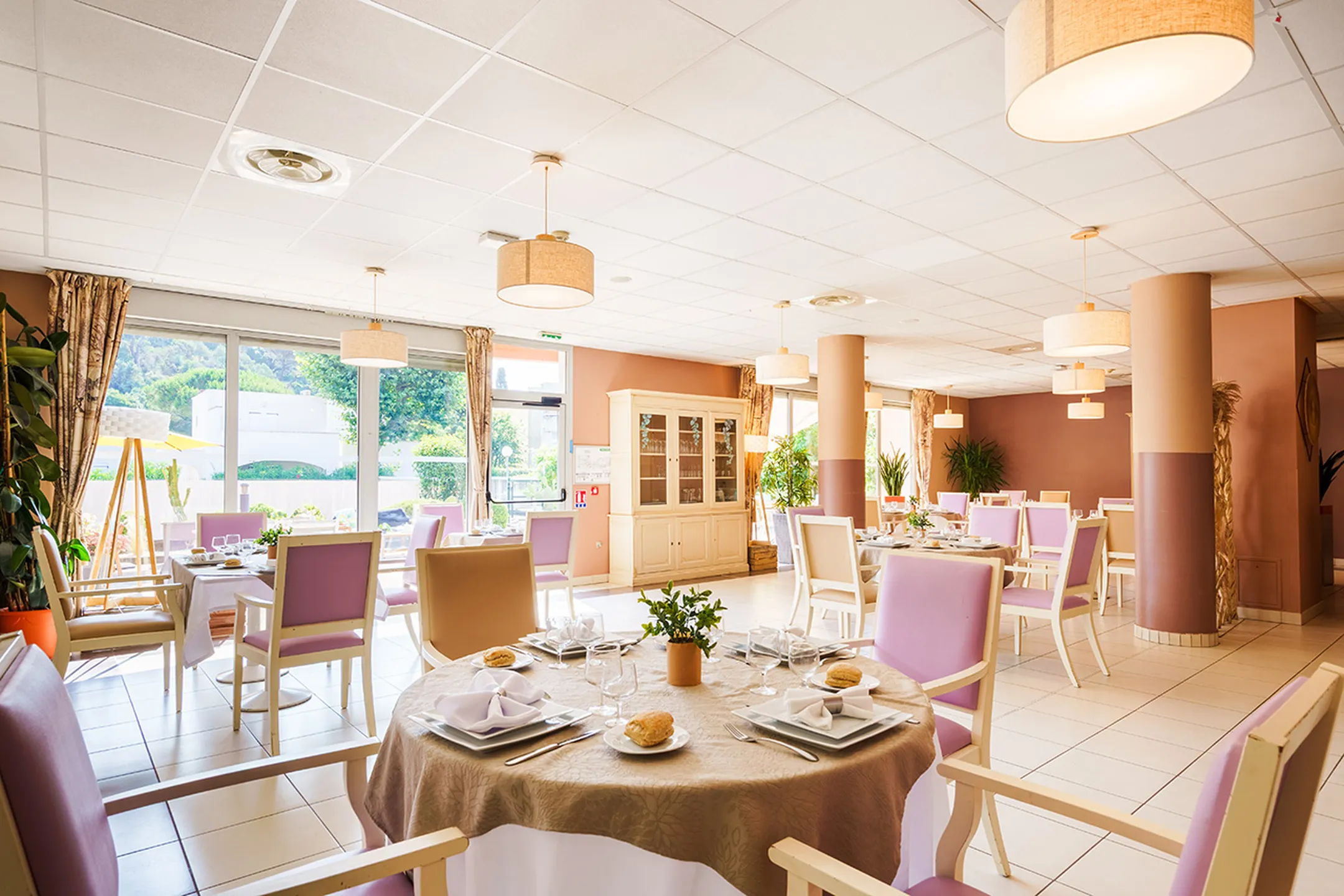Salle à manger lumineuse avec tables rondes dressées, vaisselles blanches ehpad villa saules