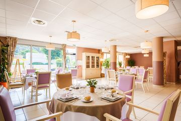 Salle à manger lumineuse avec tables rondes dressées, vaisselles blanches ehpad villa saules