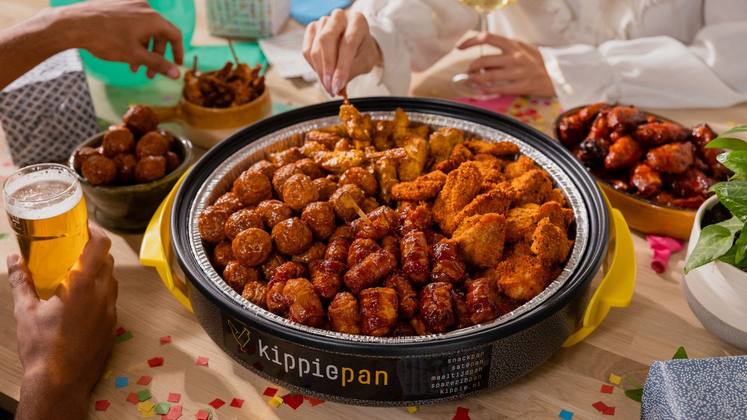 Grote Kippiepan gevuld met diverse kiphapjes zoals mini saté en kippeling op een feestelijk gedekte tafel met hapjes en drankjes.