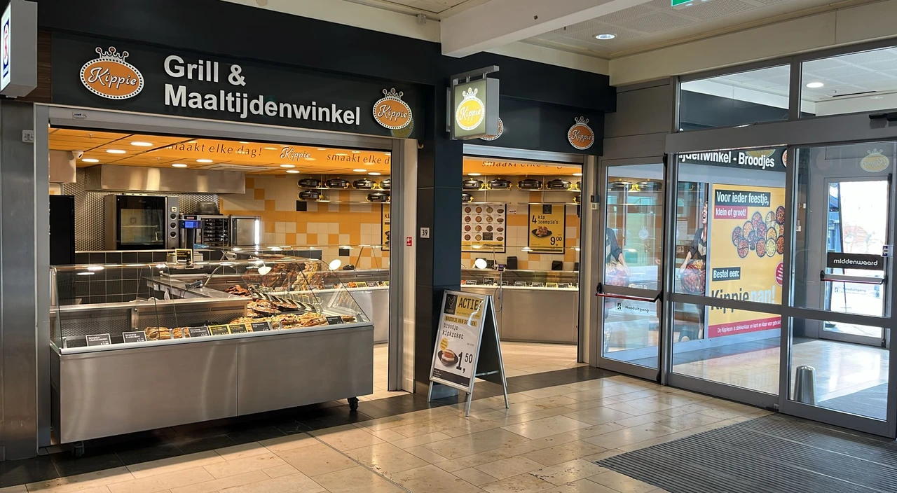 Vooraanzicht van Kippie Heerhugowaard, een Grill & Maaltijdenwinkel in een winkelcentrum, met glazen toonbanken vol gegrilde gerechten en maaltijden. Aan de gevel hangen meerdere Kippie logo’s en borden.