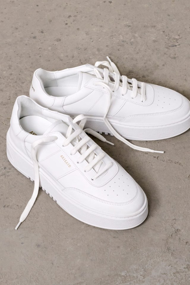 Pair of white sneakers with thick soles on a concrete floor. Laces are untied and eyelets are visible.