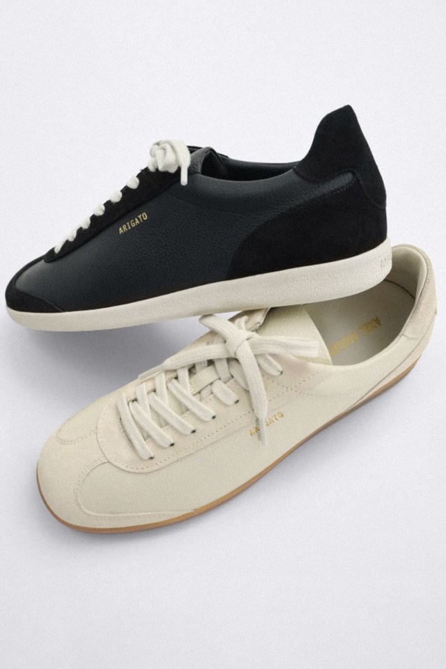A pair of casual sneakers, one black with white laces and the other cream with matching laces, both featuring "Axel Arigato" branding.