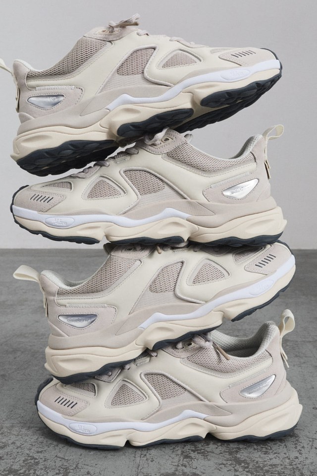 Stacked beige sneakers with mesh panels and chunky soles, displayed on a gray floor.