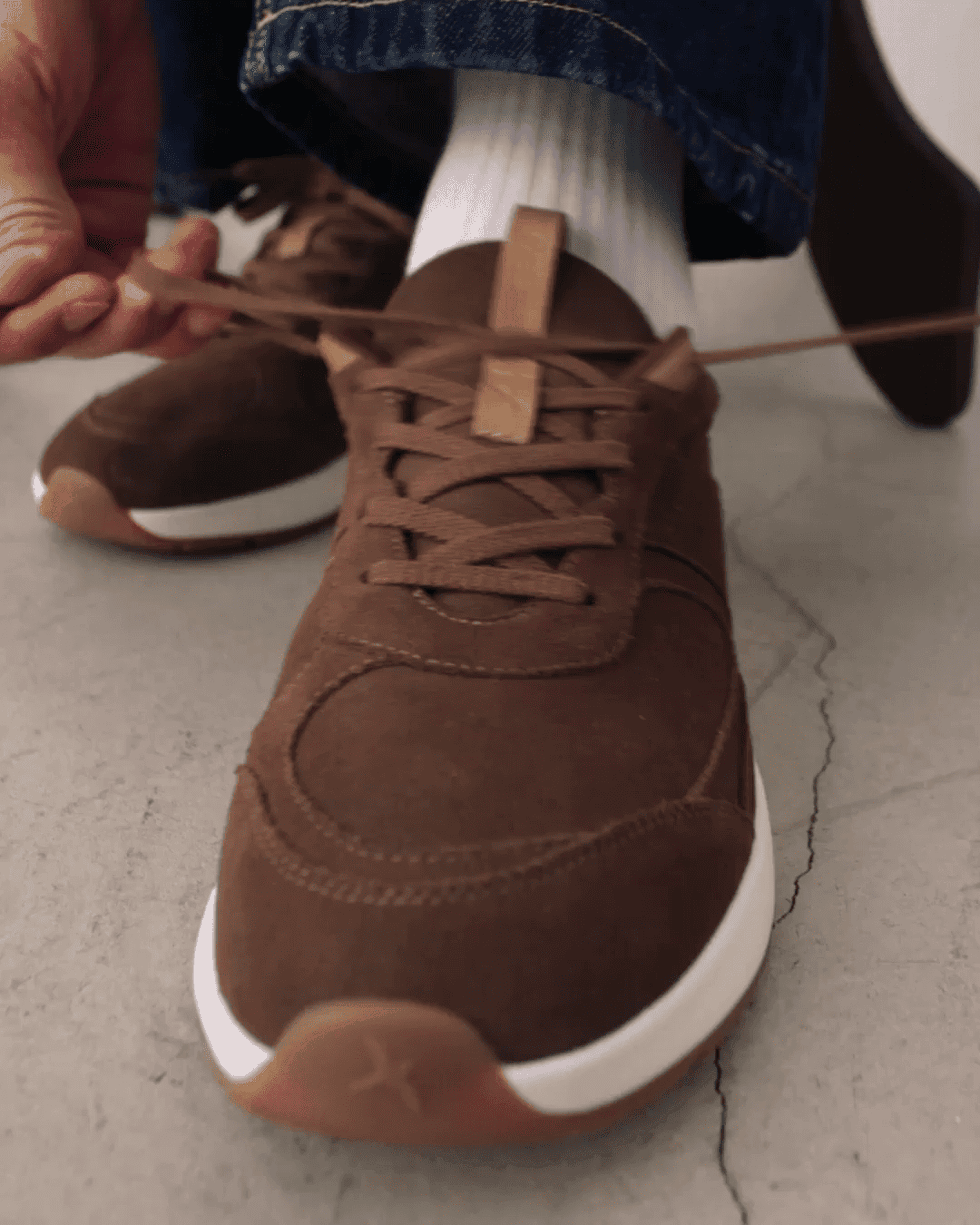 Person tying the lace of a brown sneaker on a concrete surface.