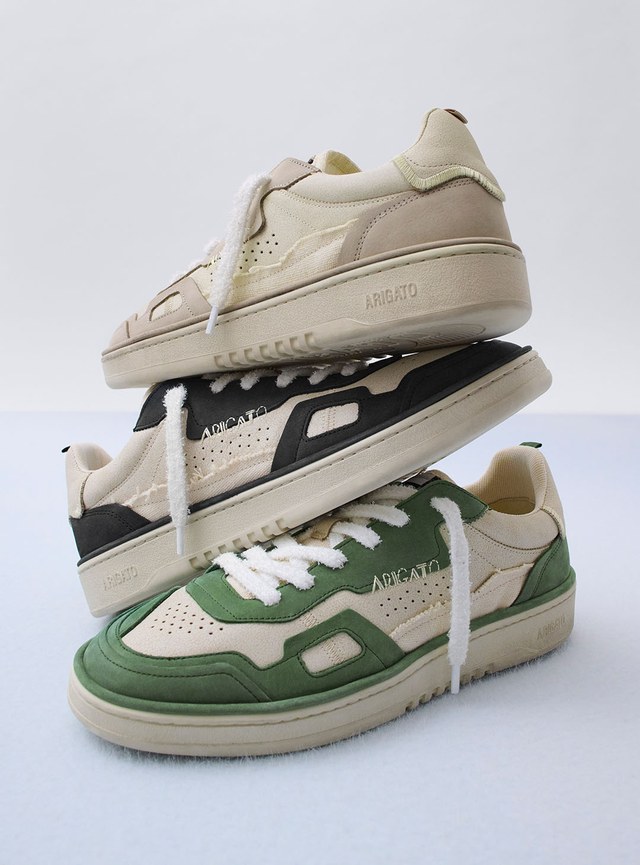 Three stacked sneakers in beige, black, and green with white laces and "Arigato" branding, displayed against a plain background.