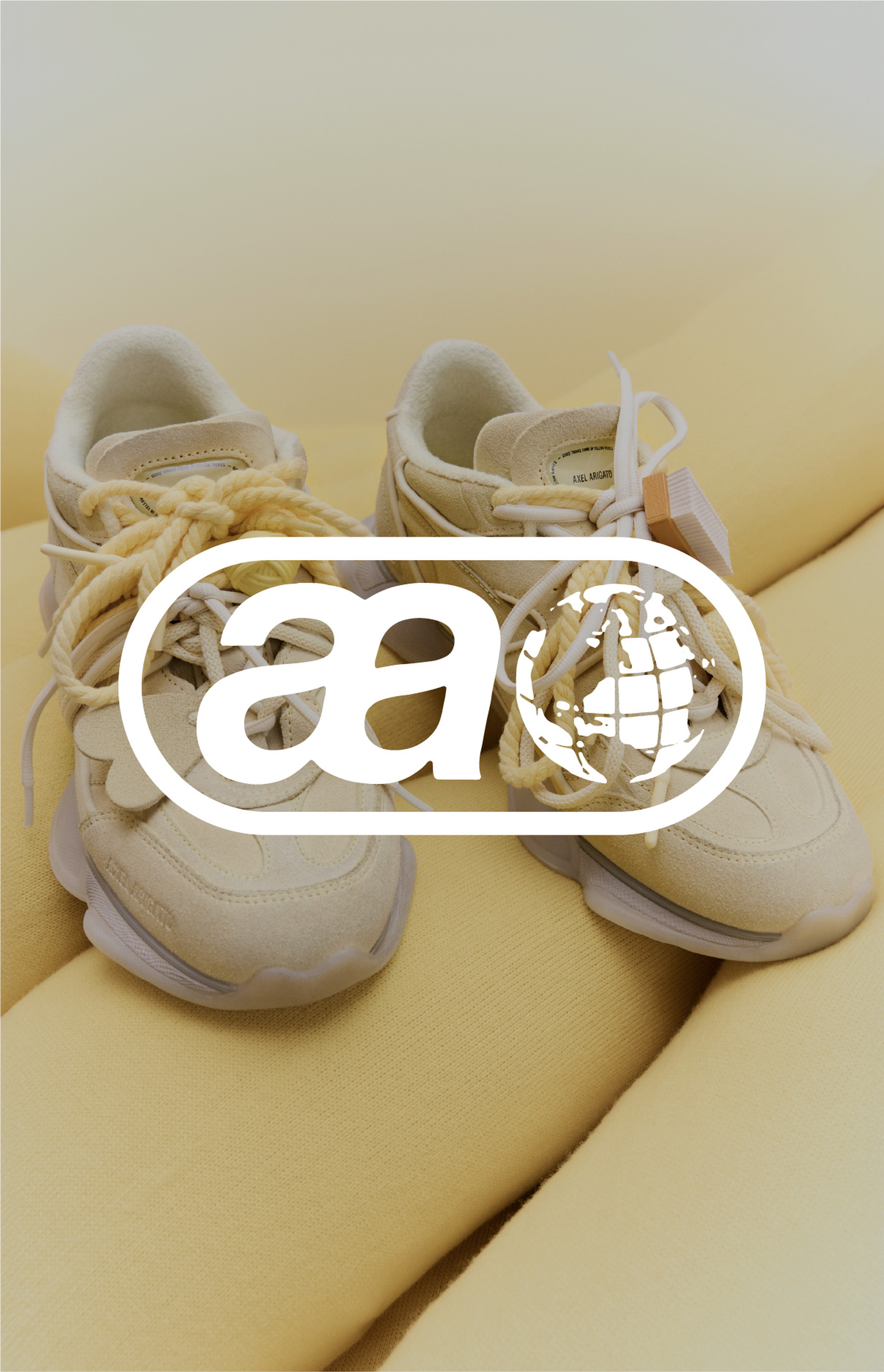 Beige sneakers with chunky soles on a soft yellow background, featuring a logo overlay of stylized letters and a globe.