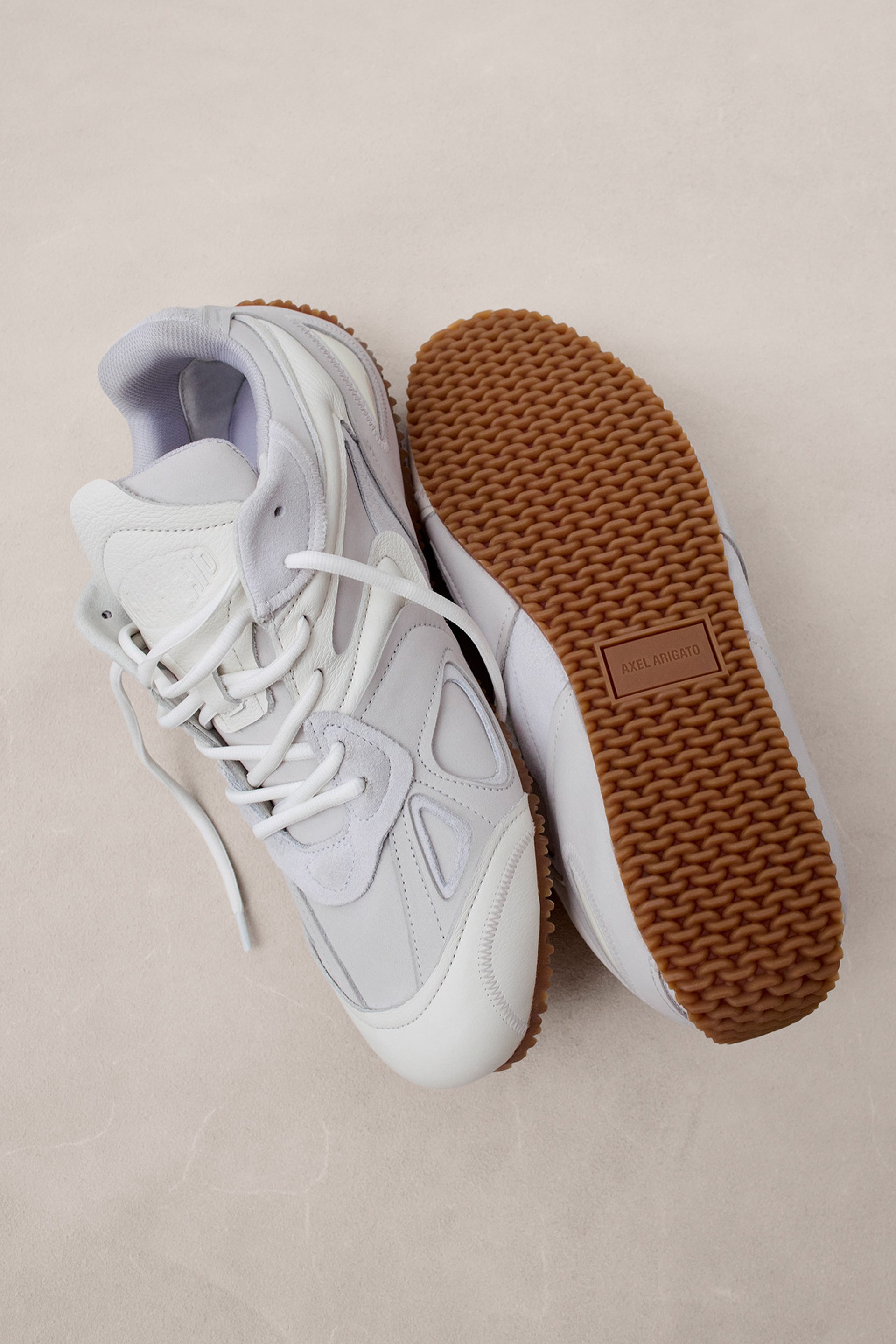 White athletic sneakers with brown textured soles, one shoe lying on its side showing the sole, and the other upright with laces visible.