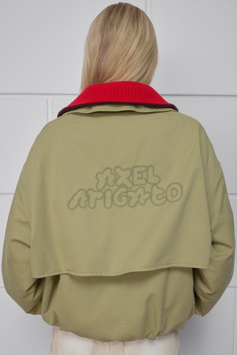 Back view of a person wearing a beige jacket with a red collar. The jacket has "AXEL ARIGATO" written on the back in a puffy font.