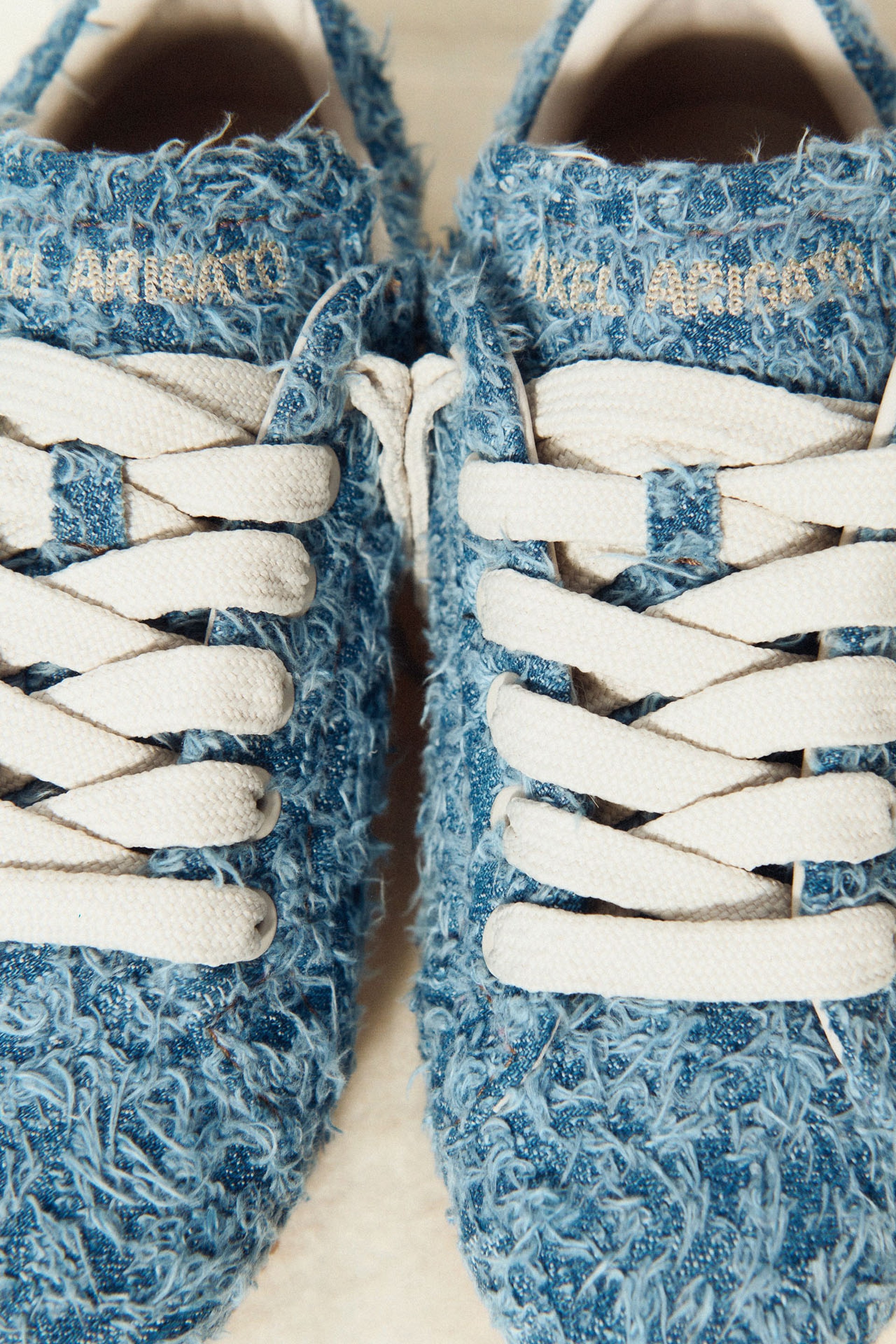 Close-up of blue textured sneakers with white laces and gold lettering on the tongue, featuring a shaggy fabric design.