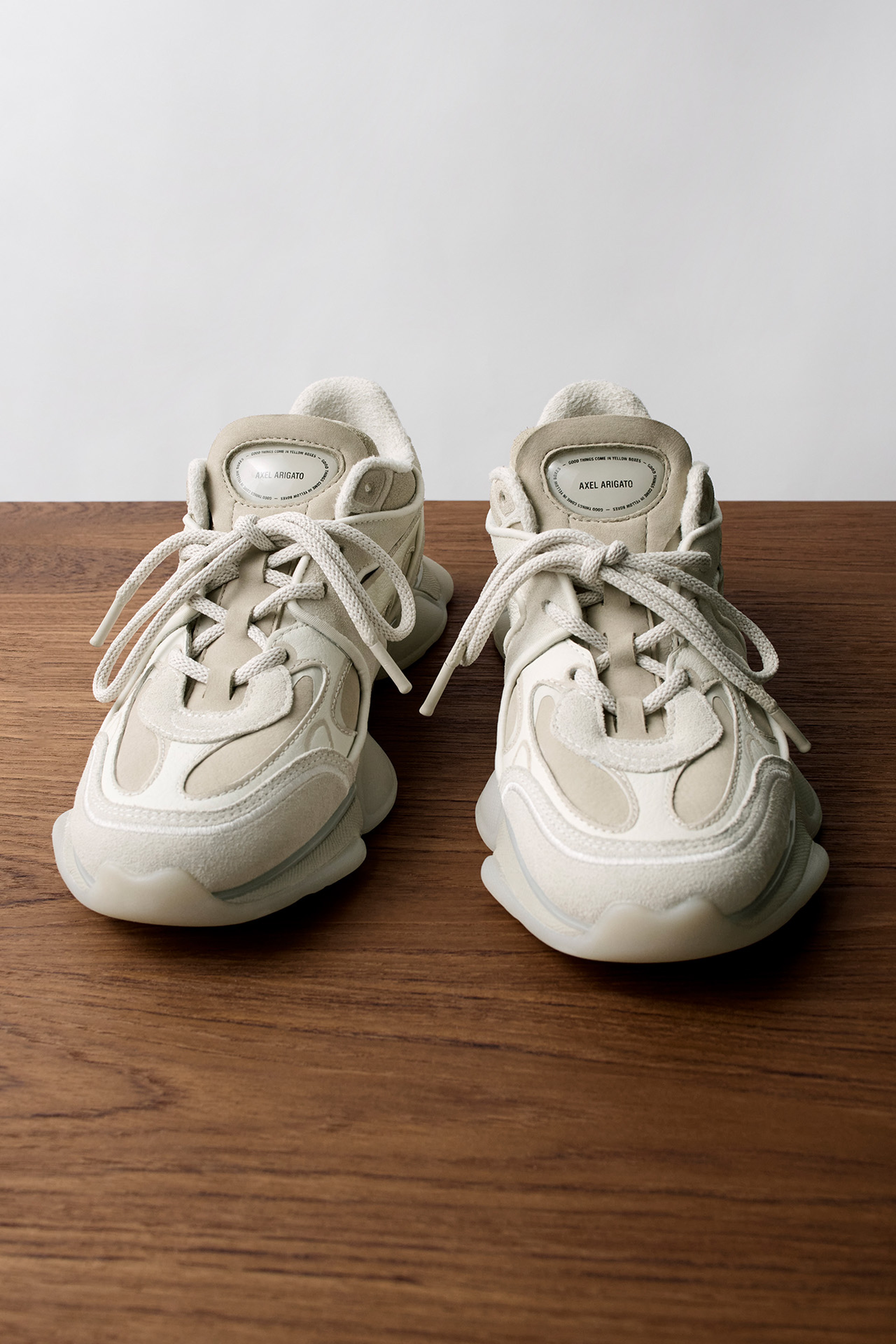 Cream-colored sneakers with chunky soles and laces, placed on a wooden surface against a plain white background.