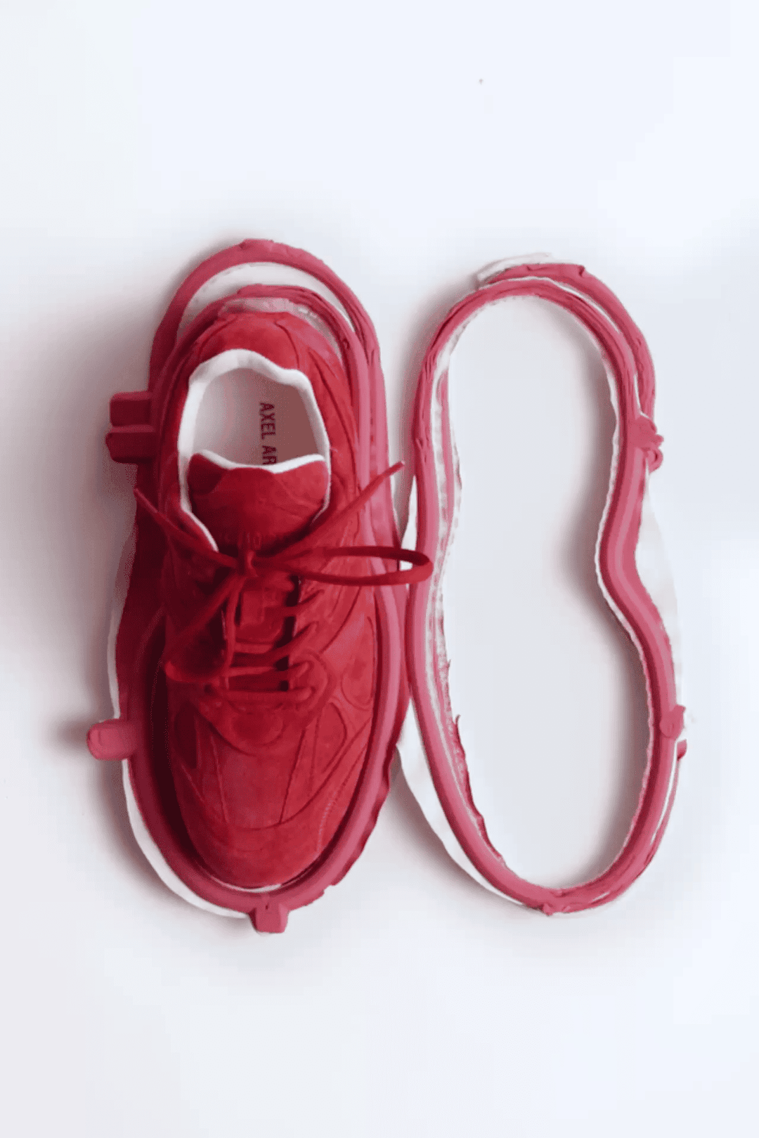 Red sneaker with its sole detached and placed beside it, showing the shoe's interior construction against a white background.