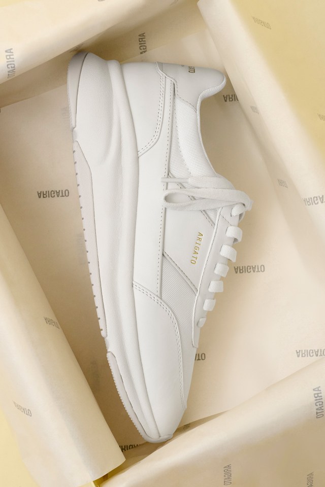 White sneaker with minimalistic design in a box, featuring a smooth leather texture and lace-up closure, placed on branded tissue paper.