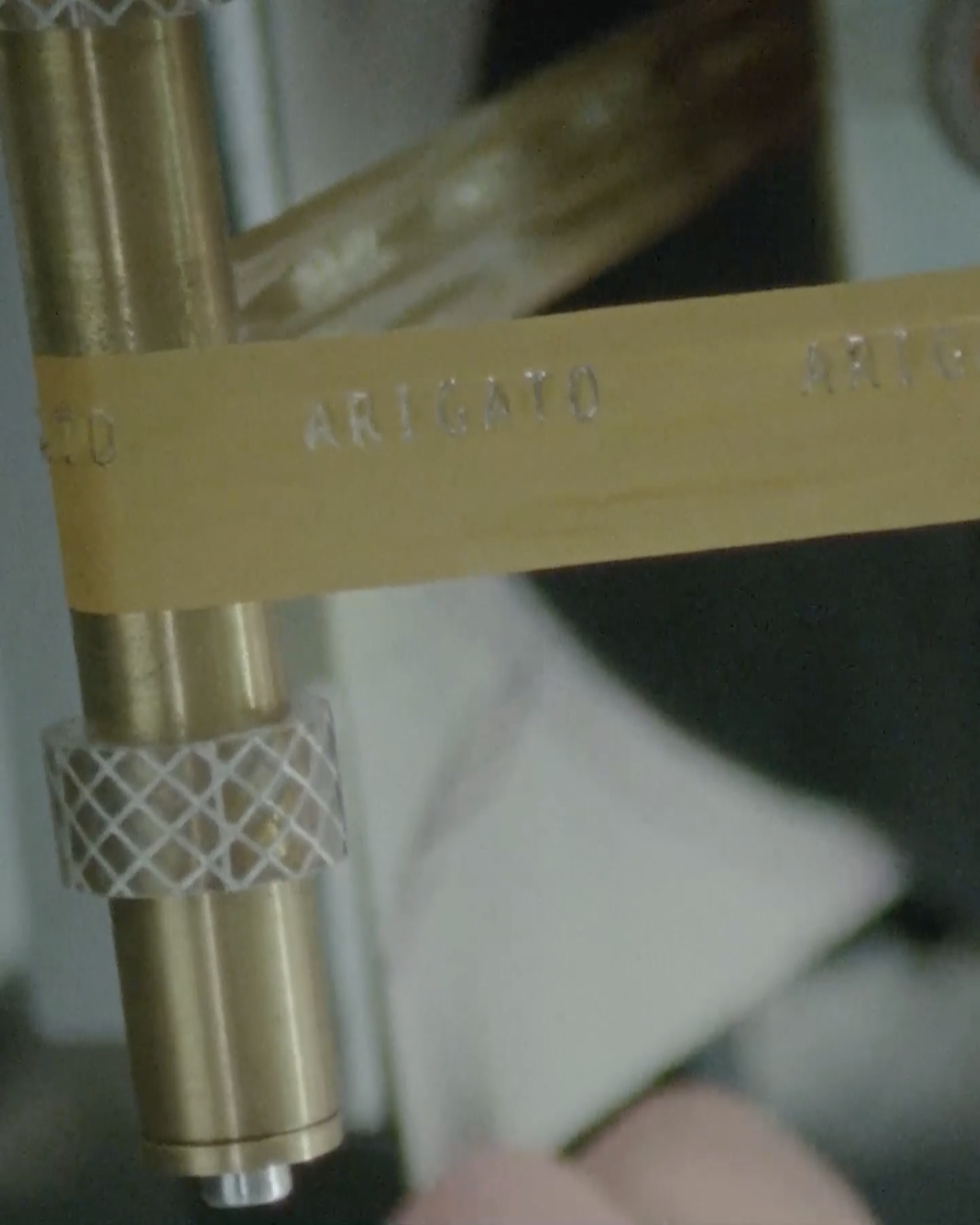 Close-up of a gold-colored tape with the word "ARIGATO" embossed, wrapped around a metallic rod with textured grips.