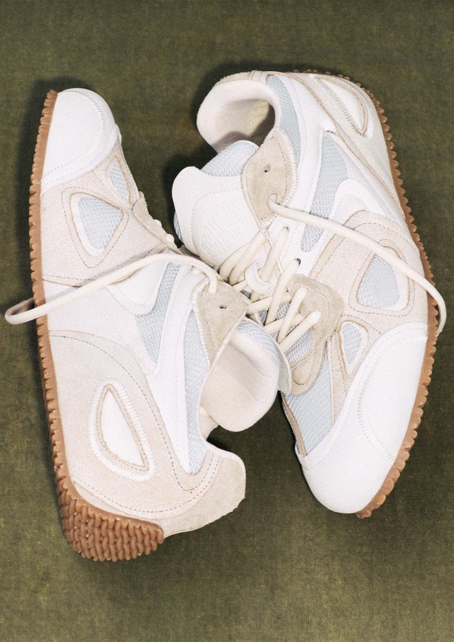 A pair of stylish beige and white sneakers with textured gum soles, displayed on a green surface.