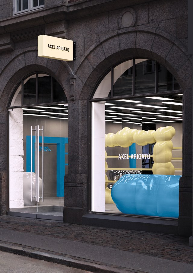 Storefront with arched windows displaying "Axel Arigato" logo. Bright blue and yellow modern decor visible inside.