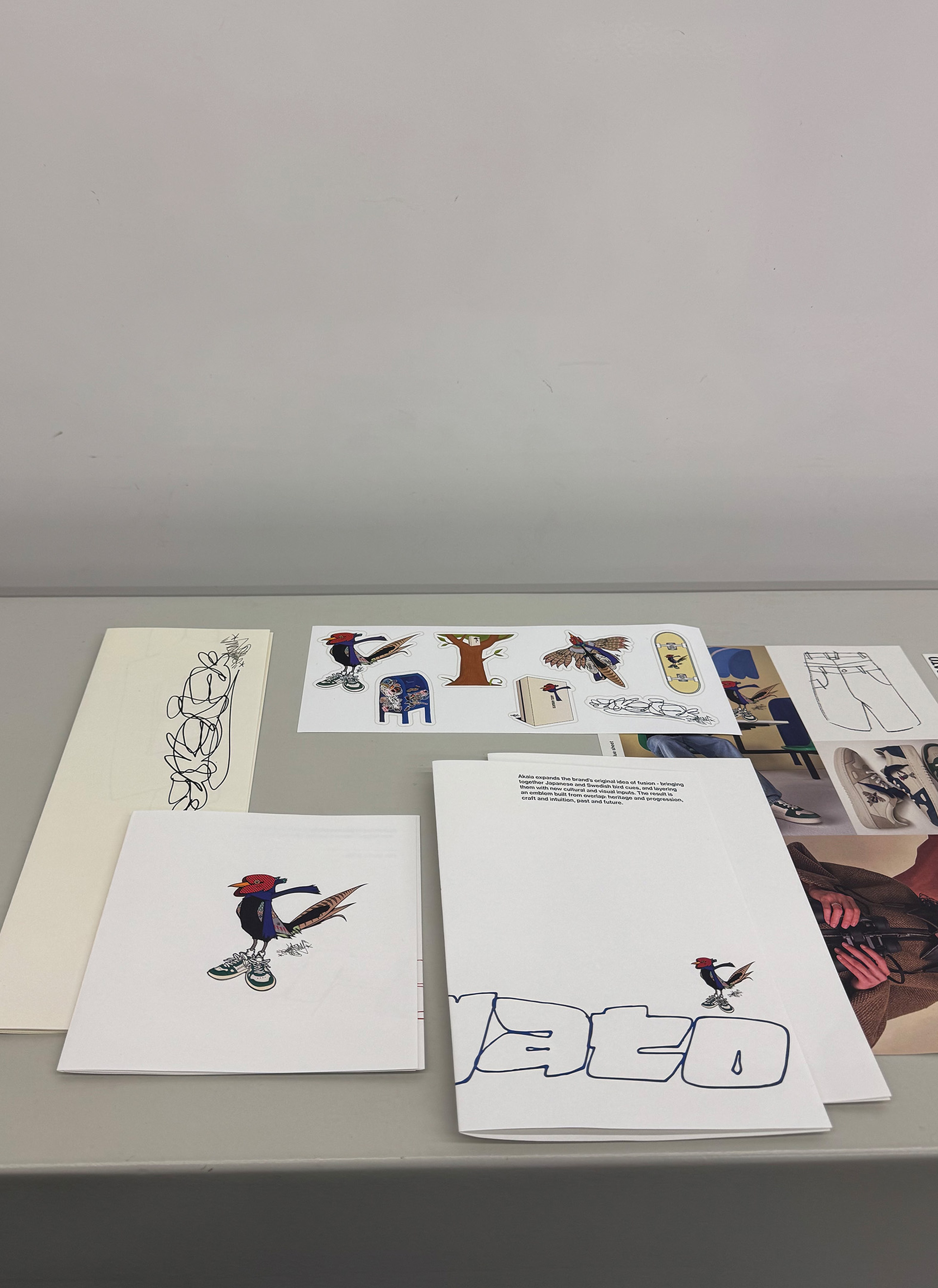Various sketch and design prints laid out on a gray surface, featuring colorful cartoon characters and artistic text.
