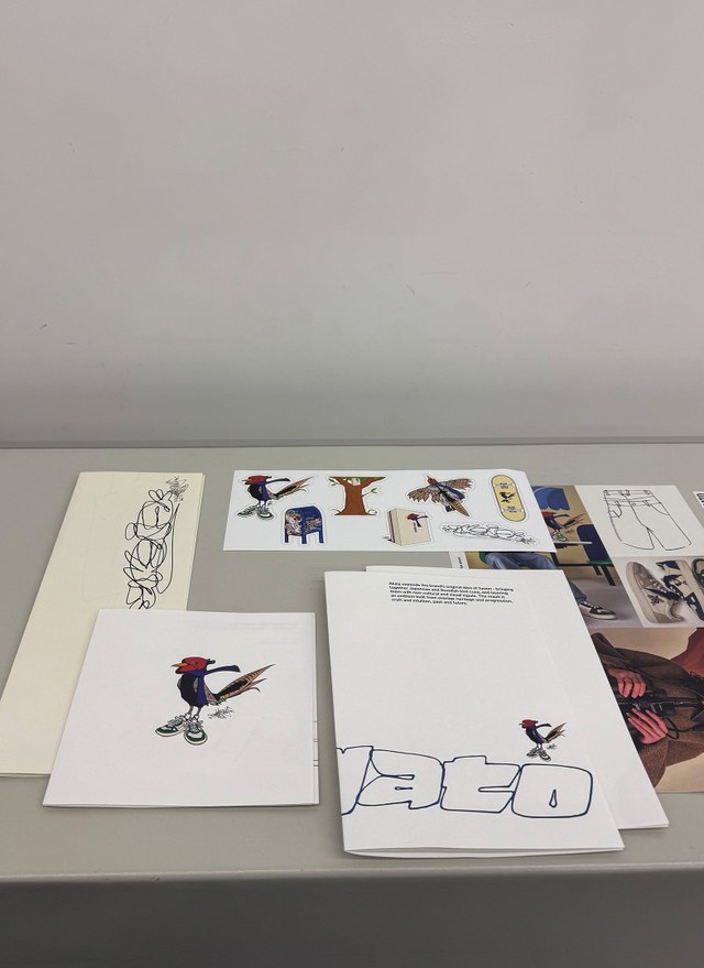 Various sketch and design prints laid out on a gray surface, featuring colorful cartoon characters and artistic text.