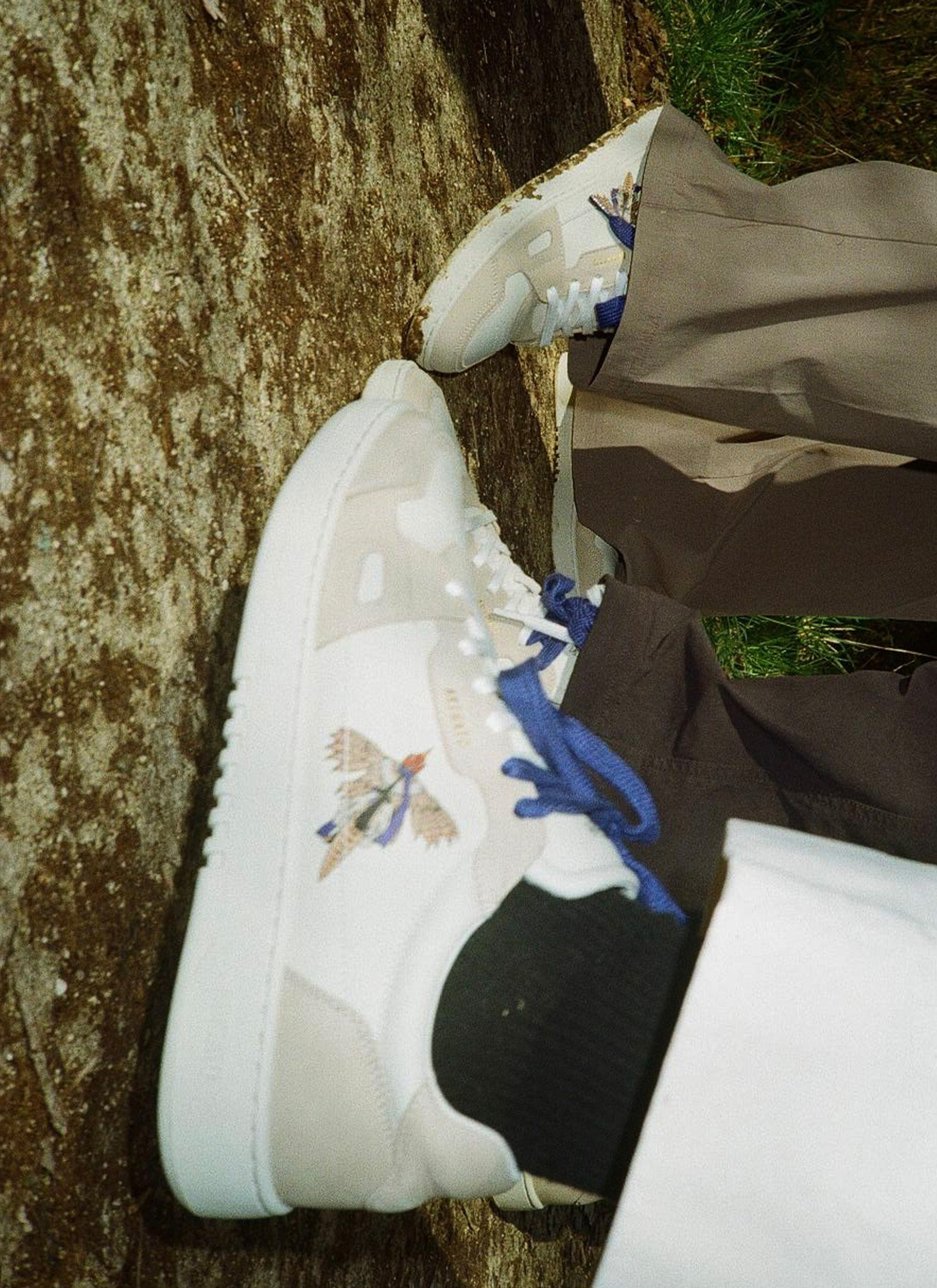 Two people wearing white sneakers with blue laces; designs of birds on the sides, standing on a stone surface.