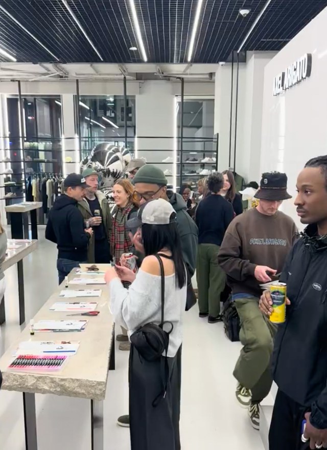 People socializing at a modern store event with tables displaying items, under bright lights and sleek decor.