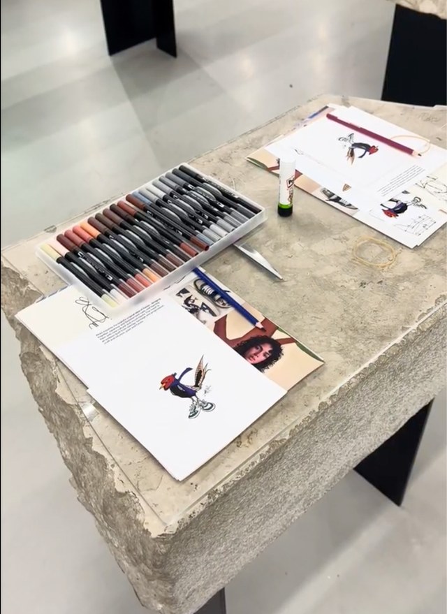 Art supplies and sketches on a stone-textured table, featuring colored pens, pencils, and artistic bird illustrations.