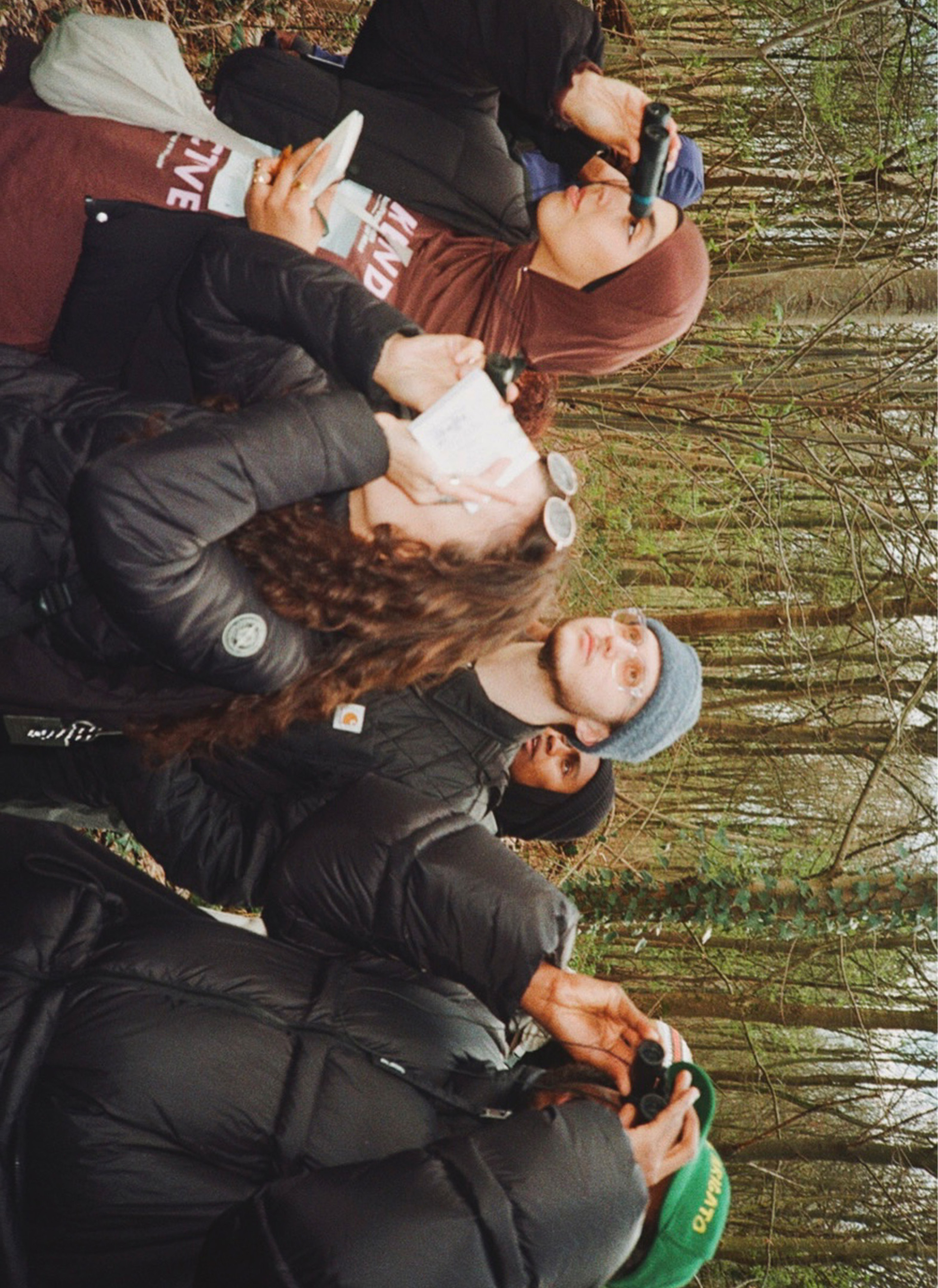 A group of people in warm clothing use binoculars to observe something in a wooded area.