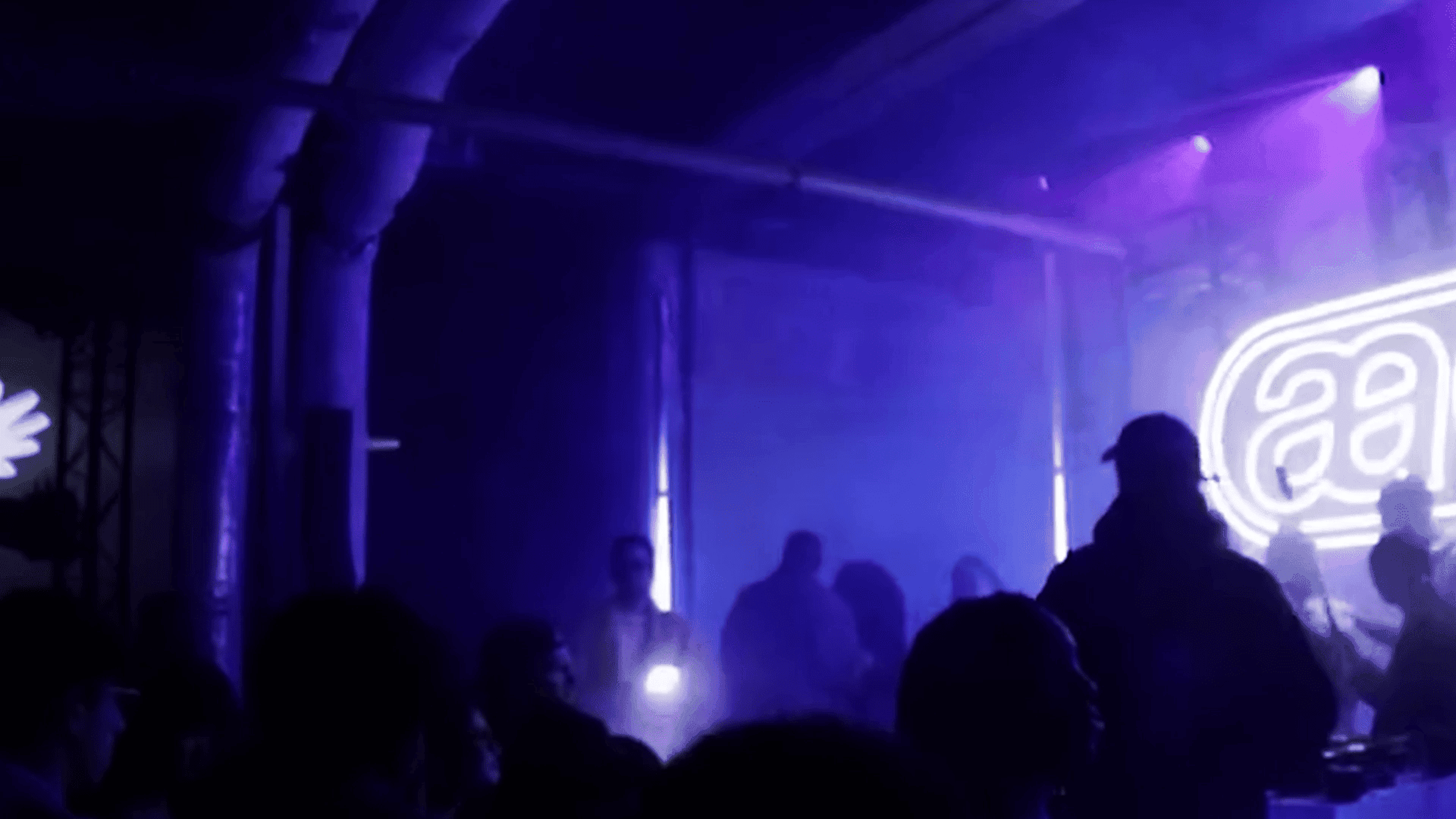 A dimly lit nightclub scene with silhouettes of people, purple lighting, and a neon sign on the wall.
