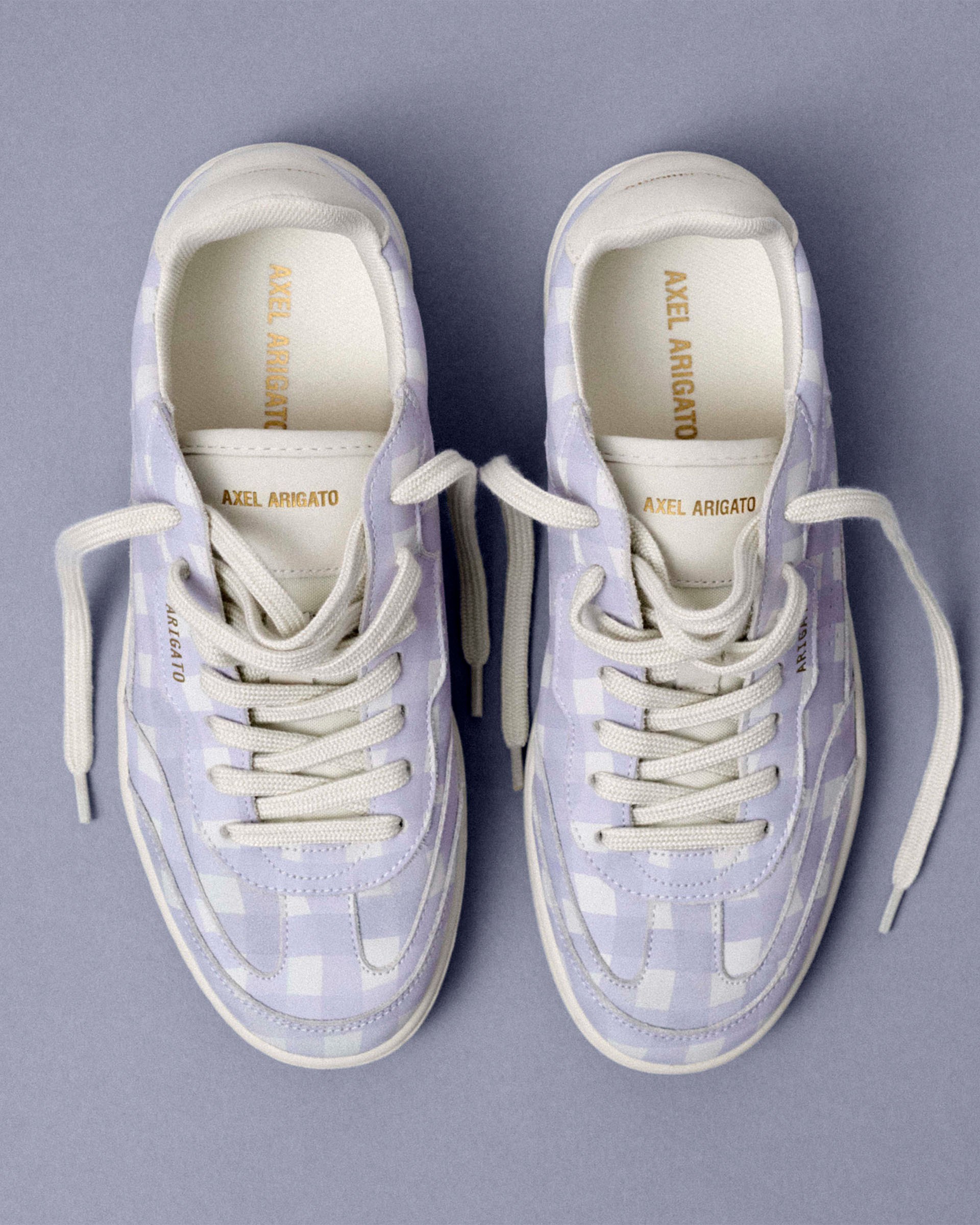 Pair of lavender checkered sneakers with white laces on a gray background.