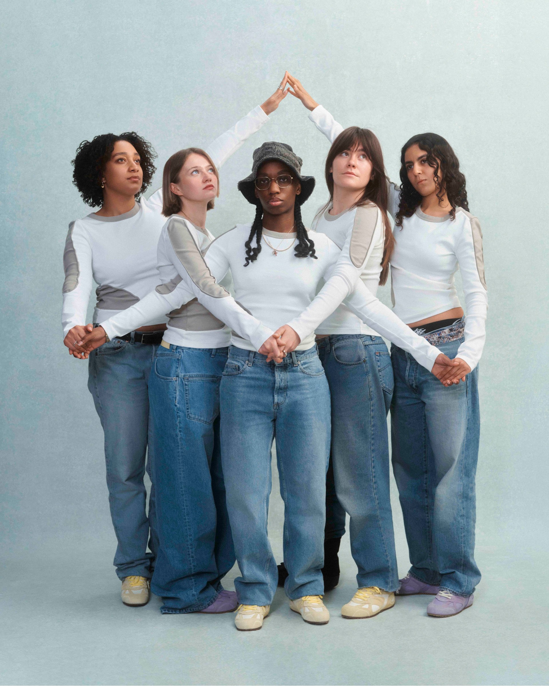 Five people in white shirts and jeans hold hands in a circle, forming a star shape with their arms, against a plain background.