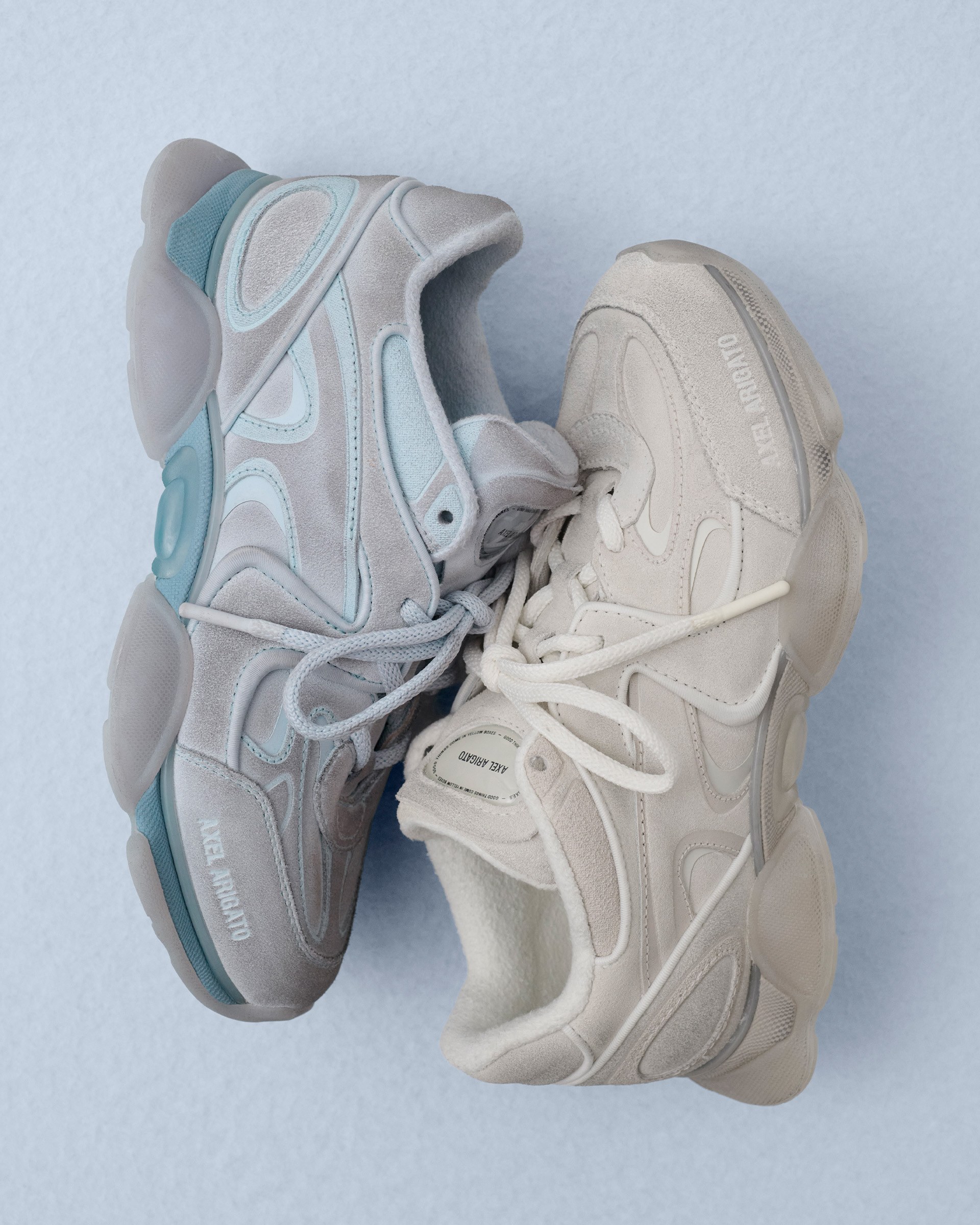 Two sneakers with chunky soles, one in light blue and the other in beige, are placed side by side on a light blue background.