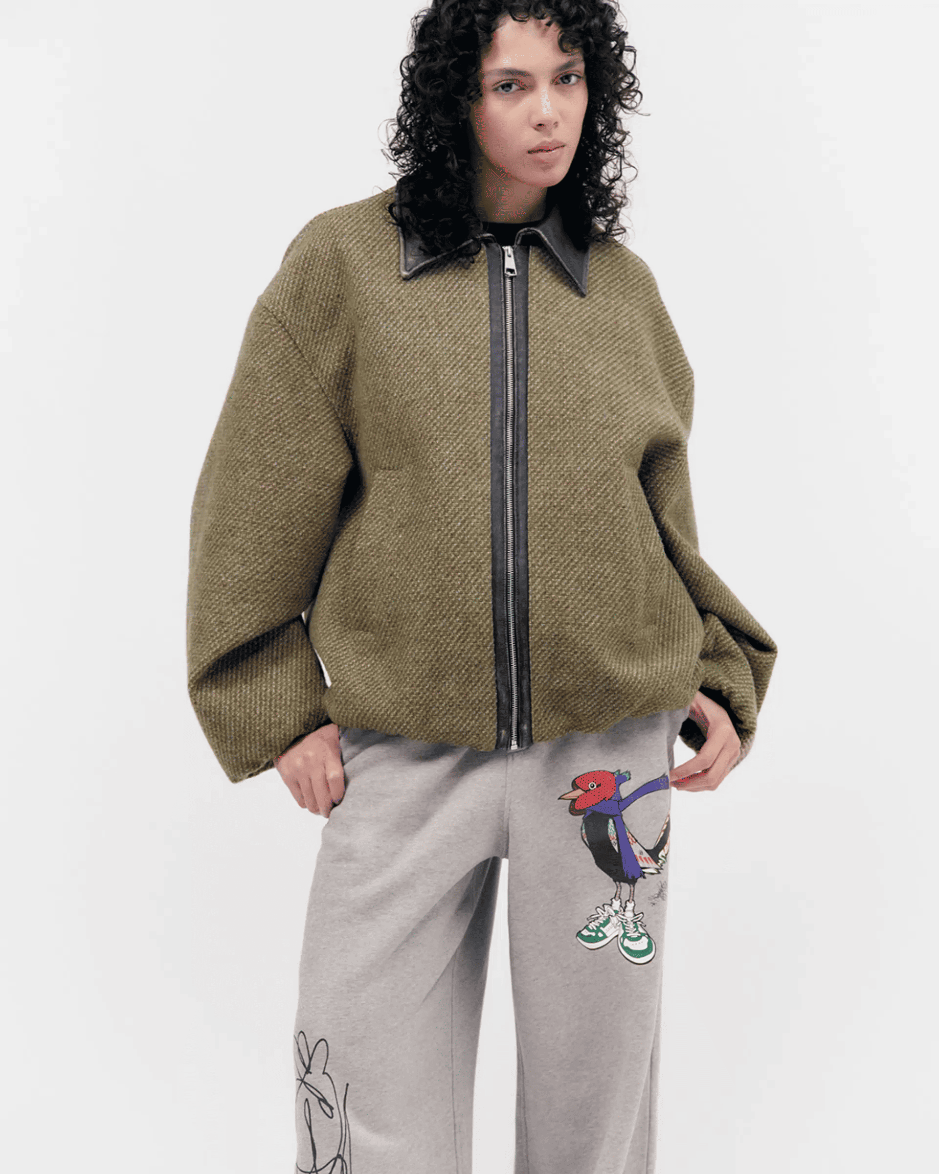 Person in a brown zip-up sweater and gray sweatpants with cartoon designs stands against a plain background.