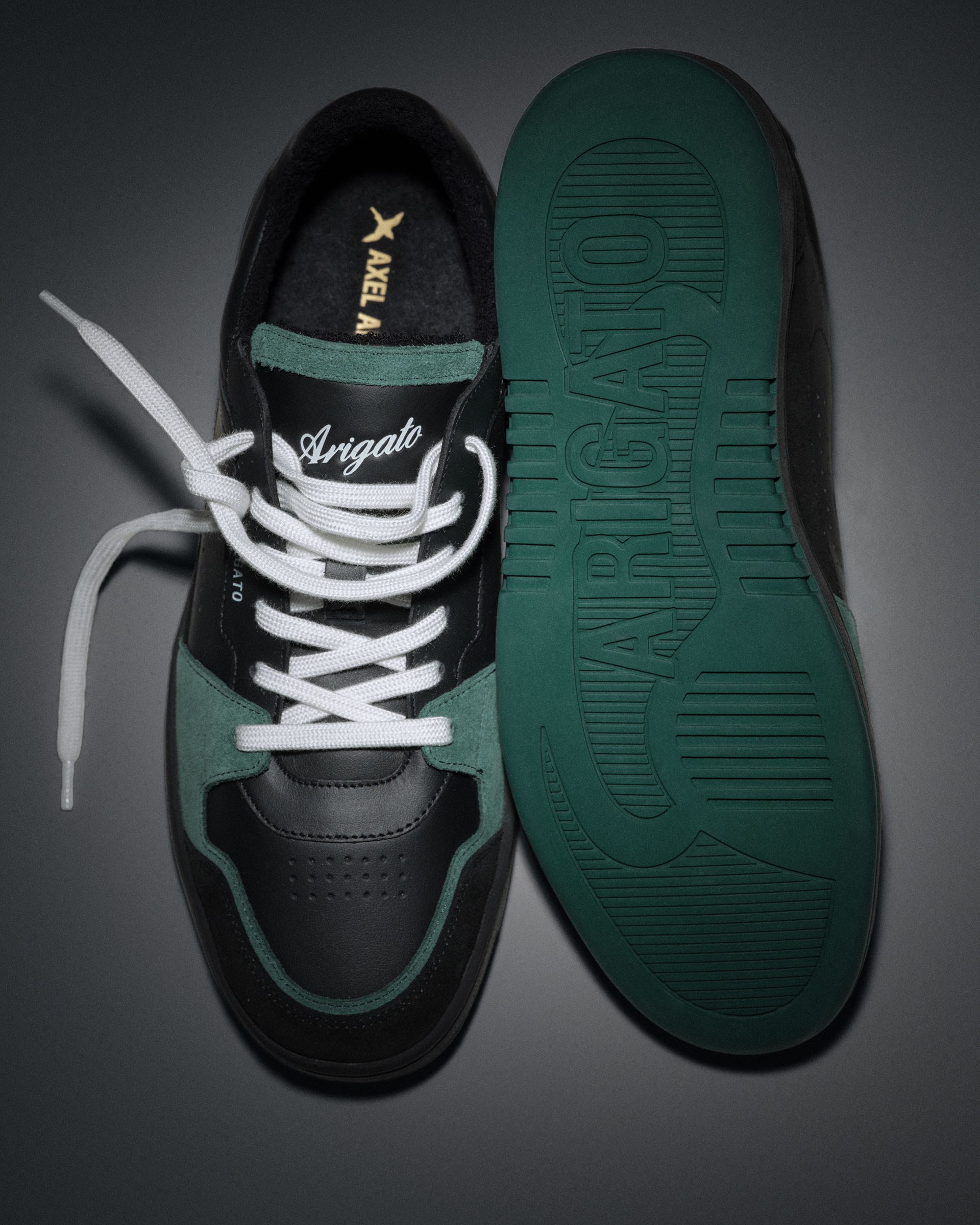 Black and teal sneakers, one top view with white laces, the other showing the sole with "Arigato" embossed, on a dark background.