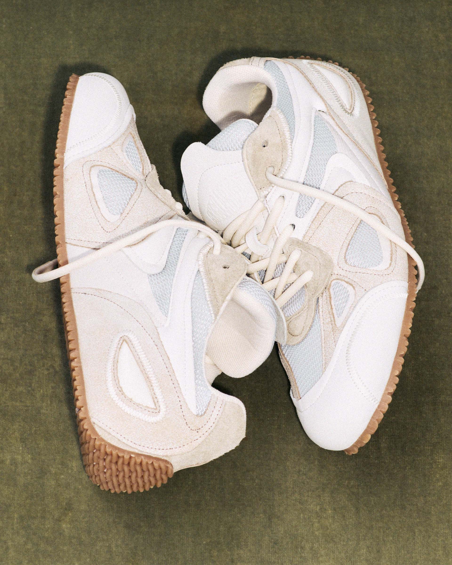 A pair of stylish white and beige sneakers with textured gum soles, featuring mesh and suede accents, on a green background.