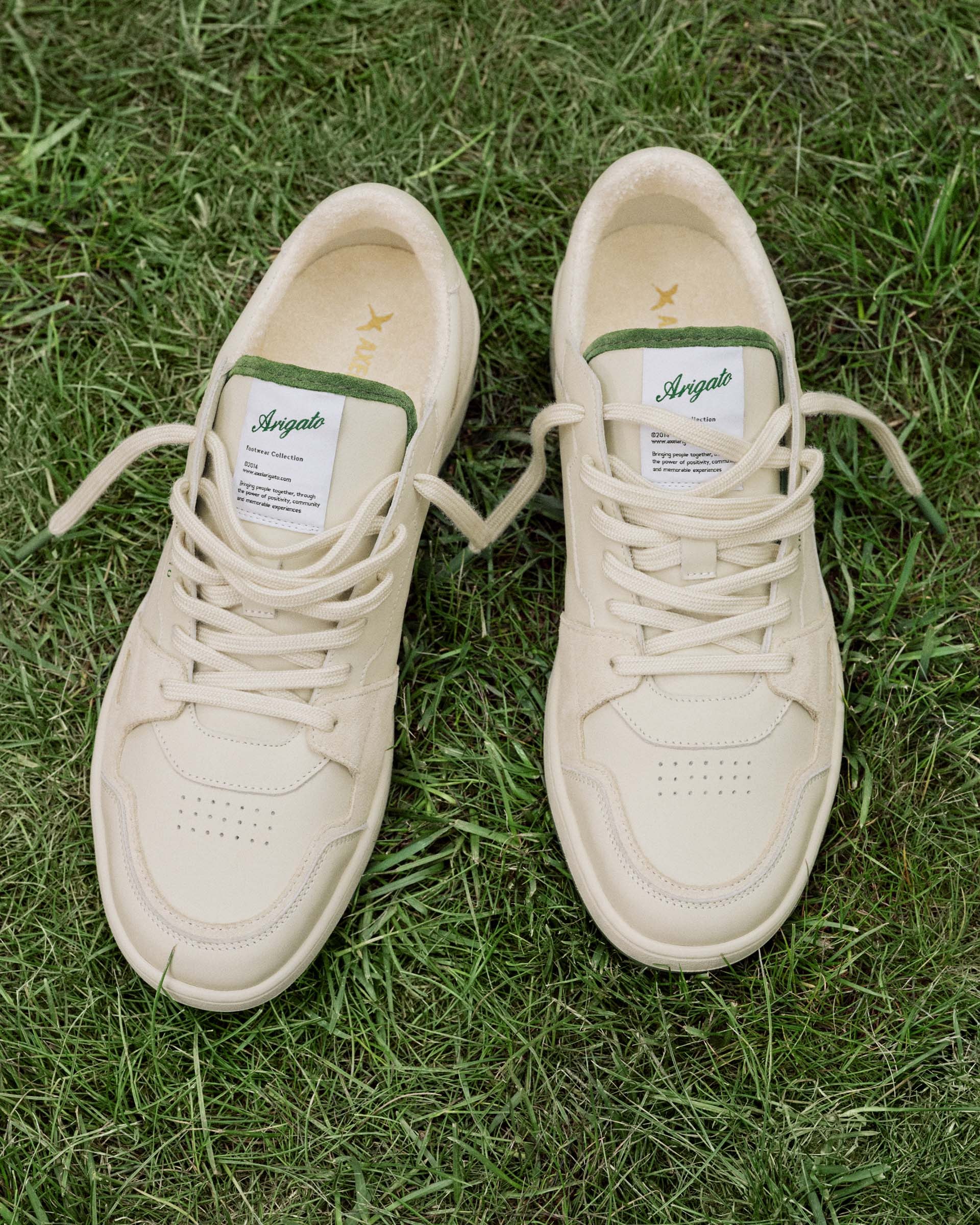 Cream-colored sneakers with green accents and laces, placed on a grassy surface.