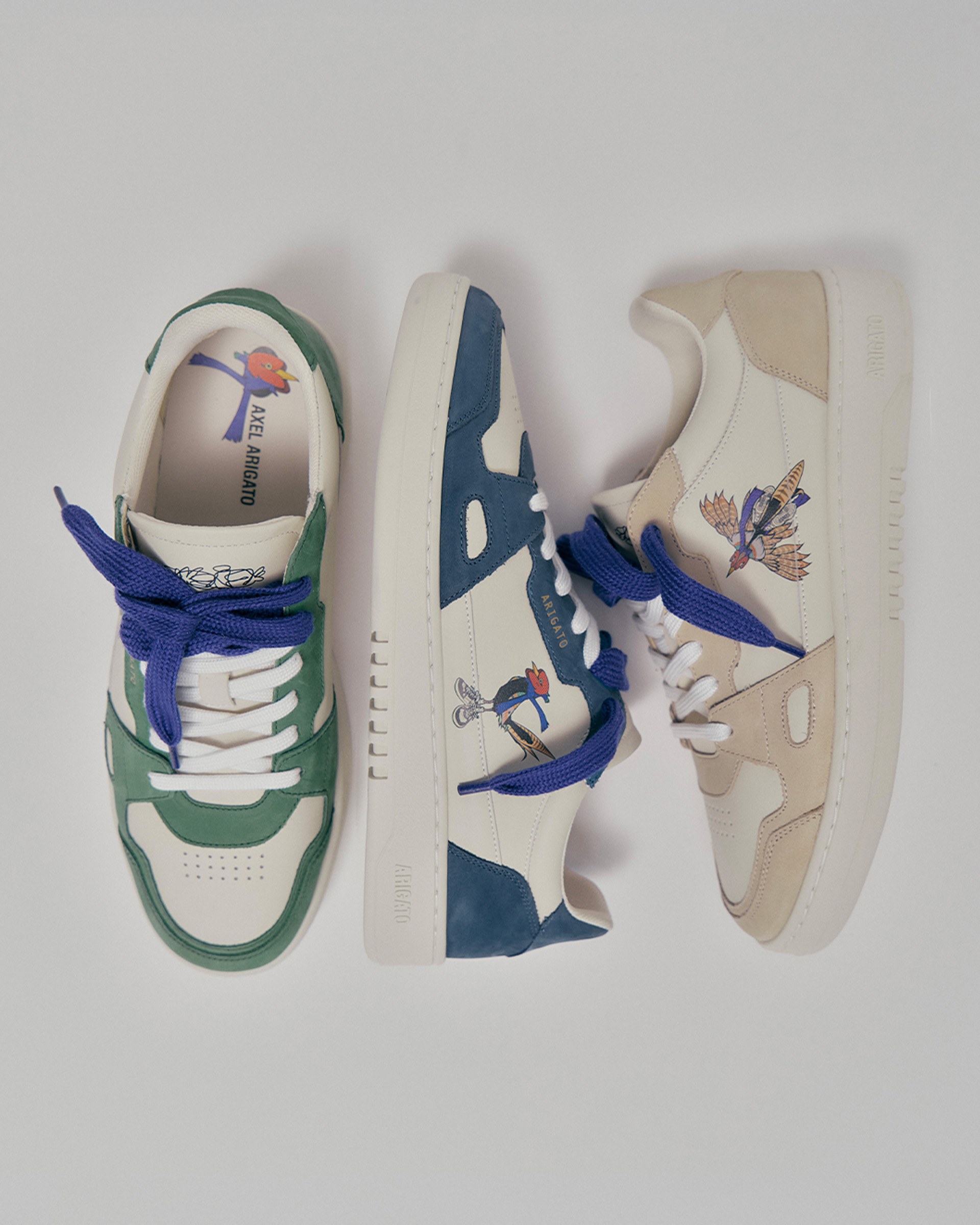 Three stylish sneakers with bird designs and colorful details, featuring green, blue, and beige accents, are arranged on a white background.