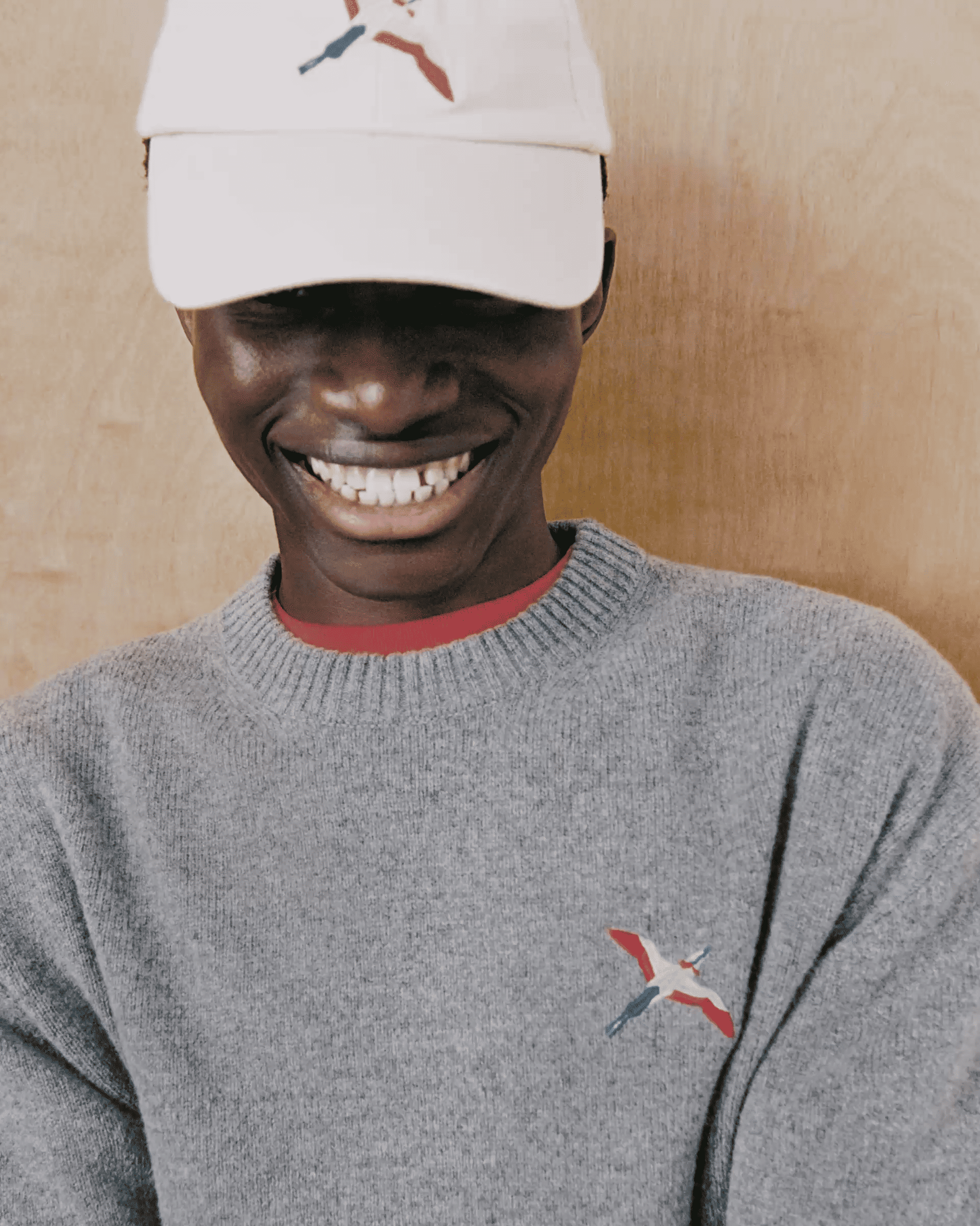 Person smiling, wearing a gray sweater and white cap, both with a colorful embroidered skier design, in front of a wooden background.